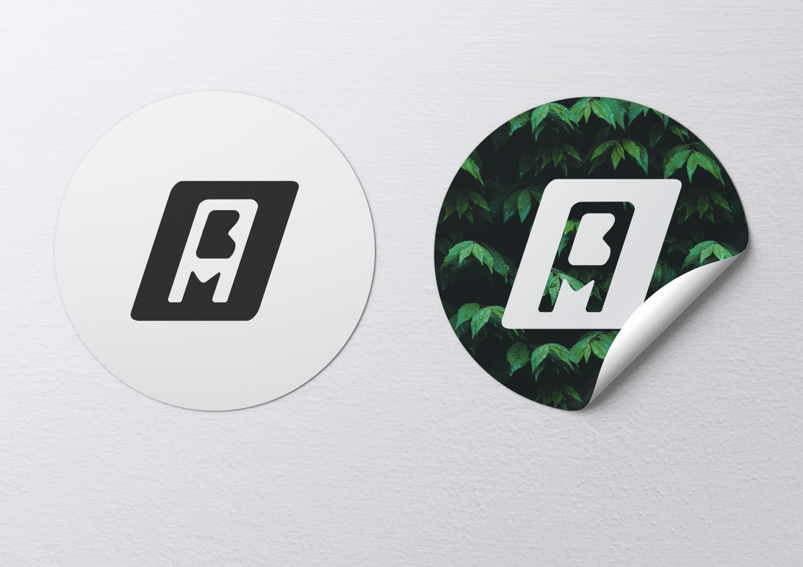 Mockup de deux stickers : l’un blanc avec le logo noir, l’autre sur fond sombre feuillu avec le logo blanc.